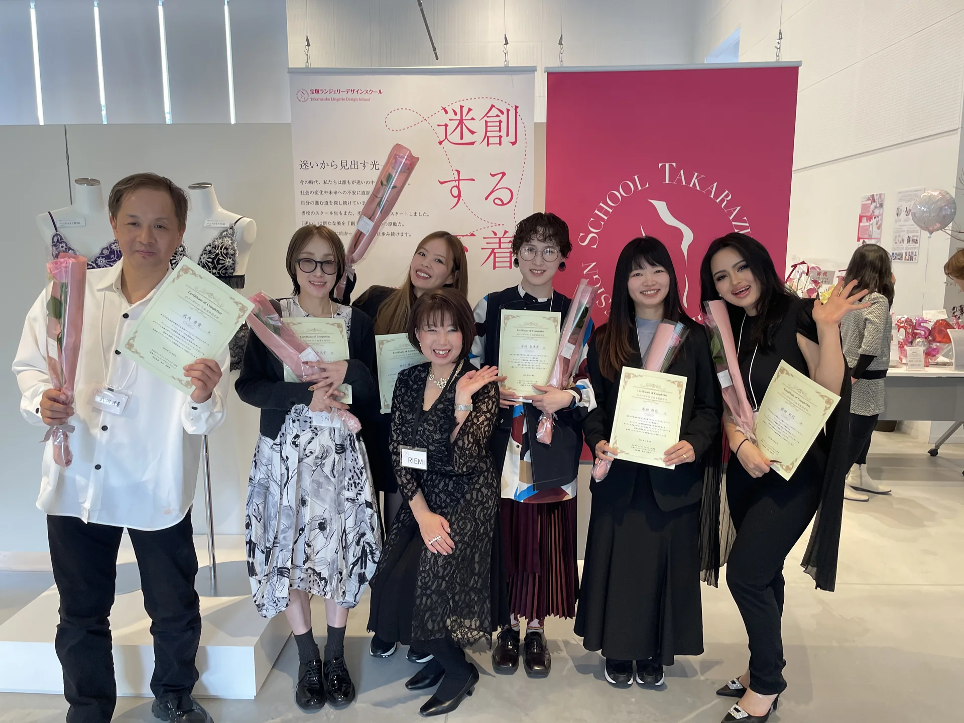 修了証書とバラを手にした受講生と講師が、宝塚ランジェリーデザインスクールのバナーの前で並ぶ集合写真